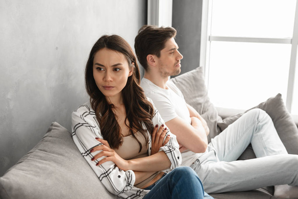 Photo of resentful guy and girl acting like arguing couple and not speaking to each other, while sitting together on couch at home isolated over white background - Valokuva, kuva