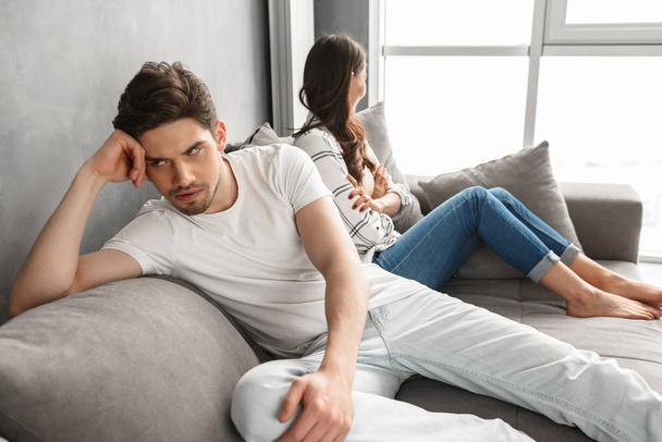 Photo of resentful guy and girl sitting together on sofa indoor with upset look and not speaking to each other isolated over white background - Zdjęcie, obraz