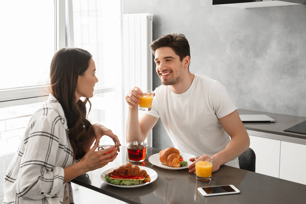 Portait of beautiful family happy man and woman having breakfast or dinner in house while sitting at table in kitchen - Фото, зображення