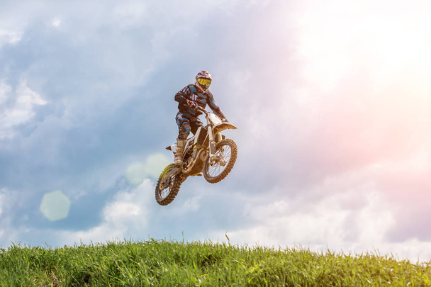 Racer na motocyklu w locie, skacze i startuje na trampolinę przed niebo. - Zdjęcie, obraz
