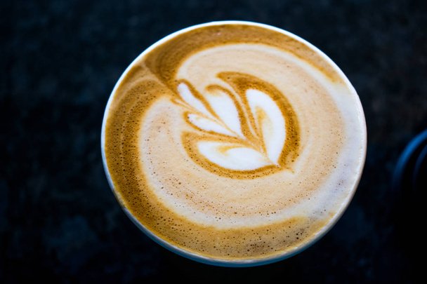 Een koffie nemen weg op een donkere achtergrond, met latte art - Foto, afbeelding