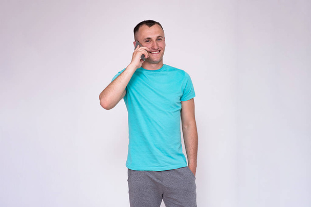 portrait of a handsome young man in a T-shirt on a white background in different poses showing in different emotions. He stands directly in front of the camera and looks into the camera - Foto, imagen