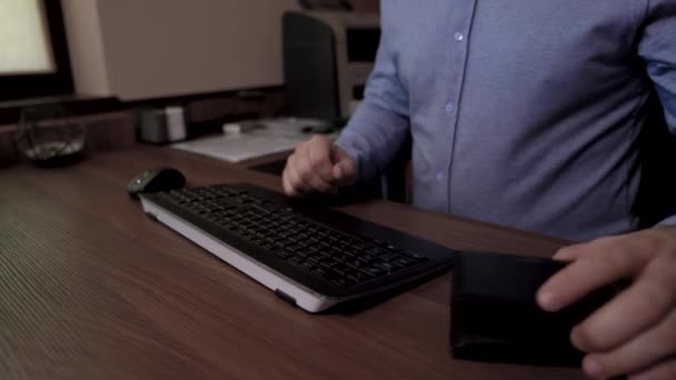 Businessman sits down at the table. Takes his credit card and starts typing on the keyboard. He uses his credit card to pay online. - Materiał filmowy, wideo