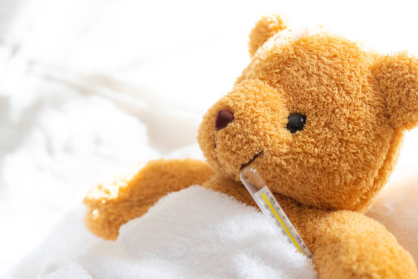 Плюшевий ведмідь хворий в лікарняному ліжку з термометром і штукатуркою. Охорона здоров'я та медична концепція
. - Фото, зображення