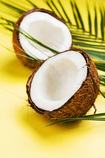Coconut halves and leaves on yellow background - Foto, afbeelding