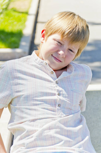 Blonde smiling boy sitting on a bench in summer park - Foto, Imagem
