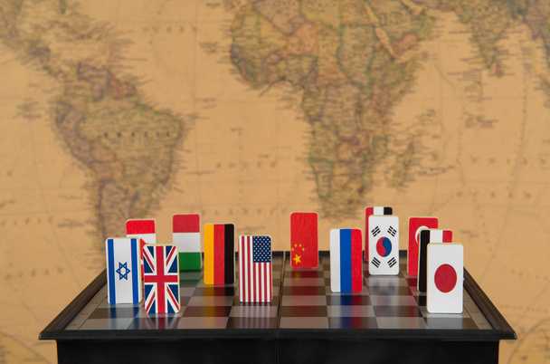 Symbole von Ländern auf dem Schachbrett vor dem Hintergrund der politischen Weltkarte. Konzeptfoto, politische Spiele.  - Foto, Bild