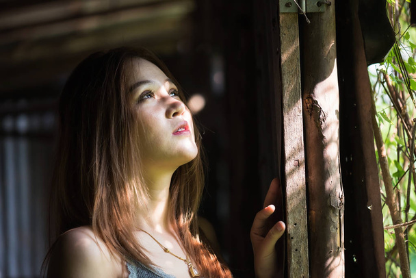 Retrato de hermosa chica asiática mirar por la ventana de madera. Mujer morena sonriente con luz de exterior con proceso de enfoque suave
 - Foto, Imagen