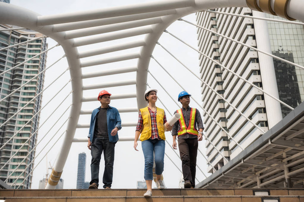 Szczęśliwy zespół inżynier azjatyckich kobiet i American kobieta zielnej w Bangkoku miasta spacerem chodnik. Międzynarodowy zespół do końca budowy budynku projektu w mieście. Koncepcja pracy zespołowej. - Zdjęcie, obraz