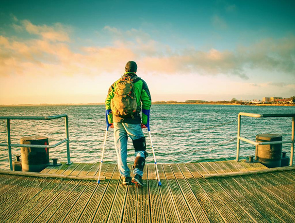 Handicap gekwetst wandelaar man is alleen bevestiging van zijn doel vieren. Toeristische staan of lopen langs op zee brug binnen het warme zonsondergang, horizon waar sky sea water raken - Foto, afbeelding
