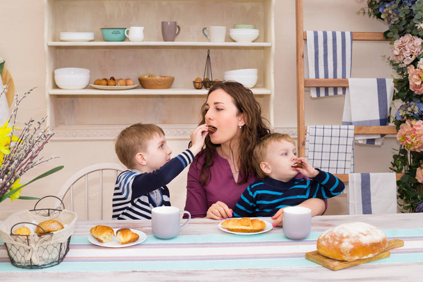 Madre y dos niños en la cocina desayunando. El hijo feliz alimenta a su madre. Madre e hijo desayunando. Concepto de familia feliz y comida saludable
. - Foto, Imagen