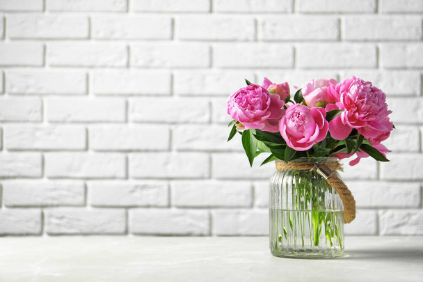 Vase with beautiful peony flowers on table against brick wall - Fotoğraf, Görsel