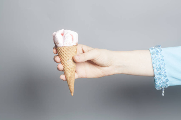 Woman hand holding an Strawberry ice cream cone on a gray background. - Foto, Bild