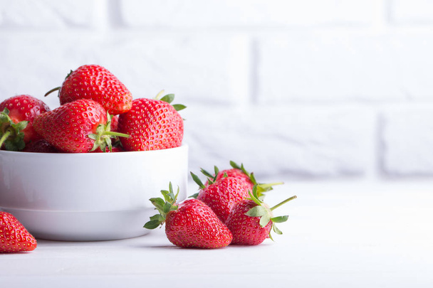 Heap of fresh strawberries in ceramic bowl on rustic white wooden background - Valokuva, kuva