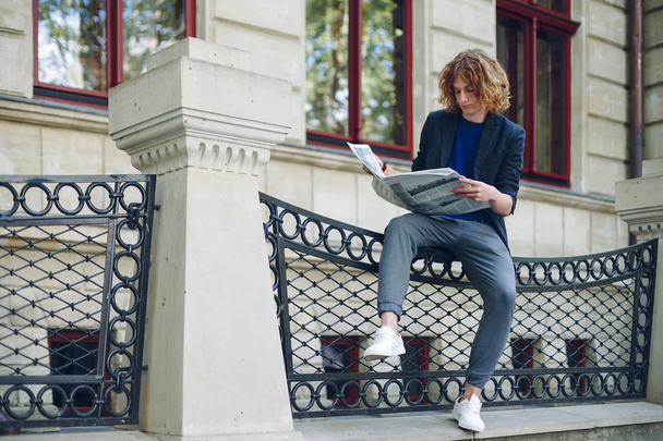 Vöröses fiatalember olvasó újság régi stílusú épület közelében - Fotó, kép