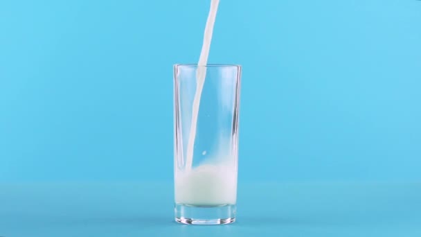 Slow motion close-up shot of milk cold beverage drink pooring into low glass blue background in studio - Imágenes, Vídeo
