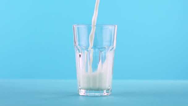 Lento primer plano de toma de bebida fría de leche pooring en vidrio facetado sobre fondo azul de color en el estudio
 - Imágenes, Vídeo