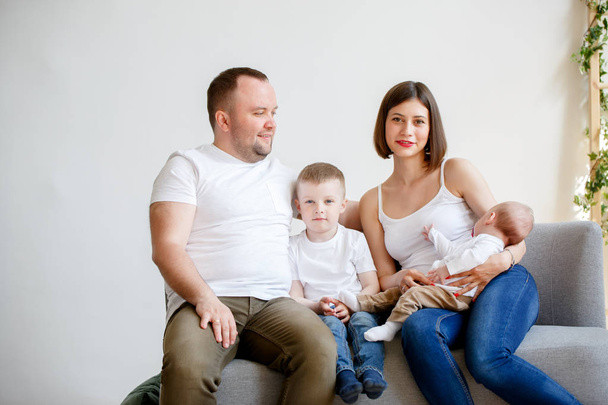 Photo of happy young parents with two small sons sitting on sofa - Fotó, kép