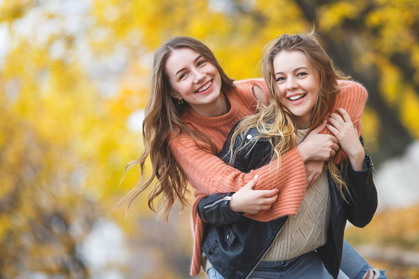 Jonge mooie meisjes, met plezier buiten in herfst achtergrond. Vrolijke vrienden in de val tijd - Foto, afbeelding