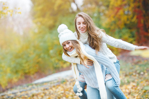 Young pretty girls having fun outdoors in autumn background. Cheerful friends in the fall time - Фото, изображение
