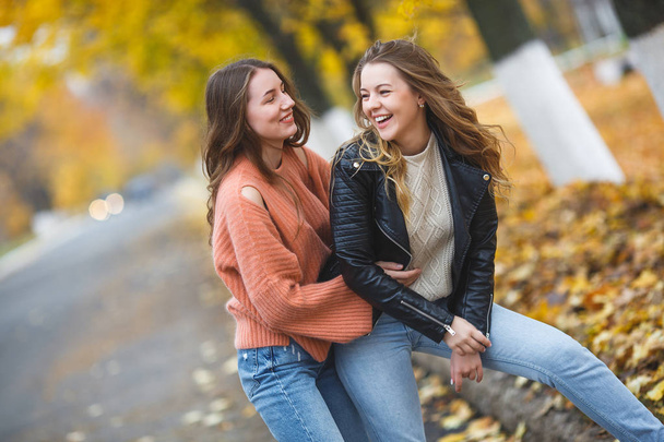 Young pretty girls having fun outdoors in autumn background. Cheerful friends in the fall time - Photo, Image