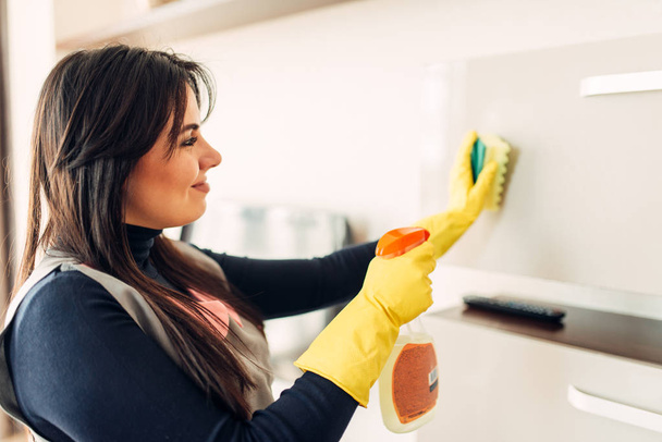Υπηρέτρια με τα χέρια σε λαστιχένια γάντια καθαρίζει τα έπιπλα με ένα σπρέι καθαρισμού. Επαγγελματική υπηρεσία οροφοκομίας προσφέρεται, παραδουλεύτρα, υγιεινής επεξεργασίας - Φωτογραφία, εικόνα