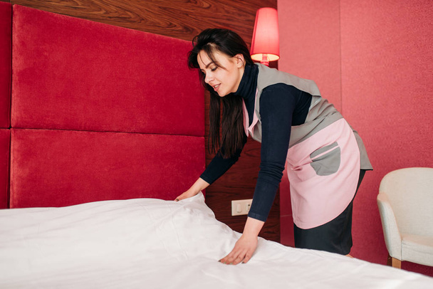 empregada bonita em uniforme fazendo a cama no quarto do hotel, serviço de limpeza, limpeza profissional
 - Foto, Imagem