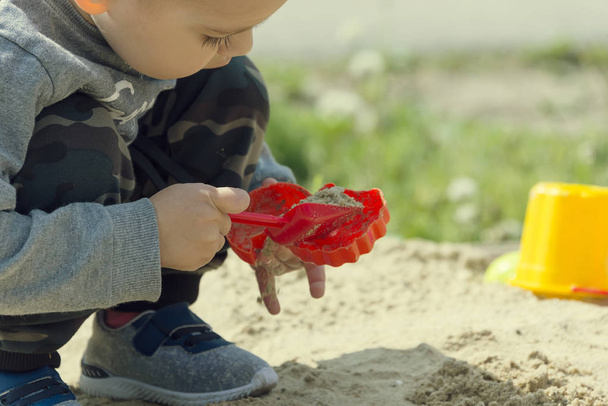 little boy playing in the sand, the child in sunny weather playing in the park on the playground - Foto, imagen