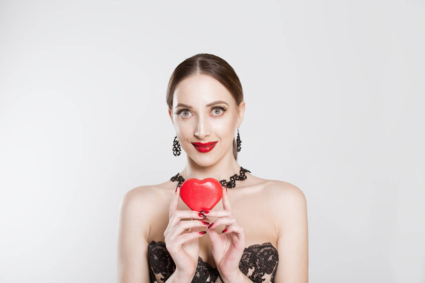 I care. Girl, beauty woman expressing love gives her heart to the lovers' day, at St. Valentine she looks expressively on white gray background. Brunette model in sexy lace dress and red lipstick lips - Photo, Image