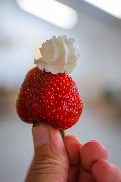 doigts tenant une fraise avec de la crème fouettée
. - Photo, image