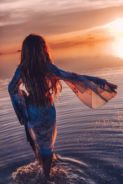 όμορφη νεαρή γυναίκα με φόρεμα ΕΛΕΓΑΝ περπάτημα στο νερό στο ηλιοβασίλεμα - Φωτογραφία, εικόνα