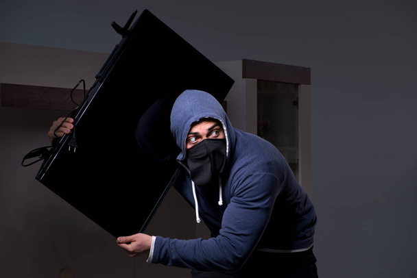 Burglar thief stealing tv from apartment house - Фото, изображение