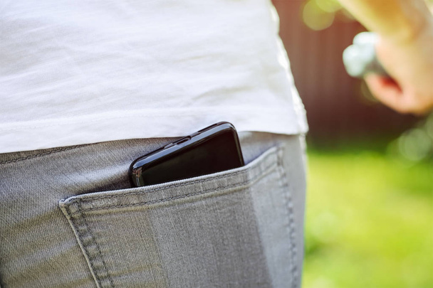Black mobile phone in back pocket of gray jeans - Zdjęcie, obraz