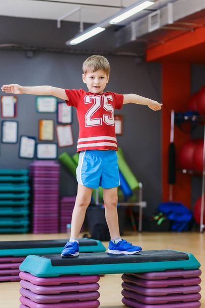 a boy in a red t-shirt stands, spreading his hands to the sides in the gym - Foto, Imagem