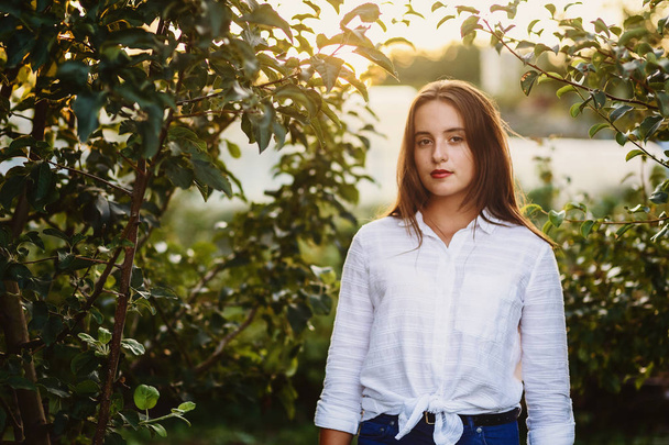 portrait of beautiful teenage girl in white blouse in Apple orchard in summer - Фото, изображение