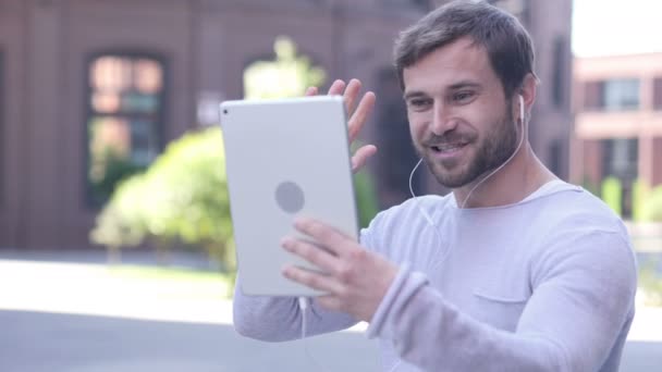 Online czat wideo na tablecie przez przystojny mężczyzna stojący poza godzinami - Materiał filmowy, wideo