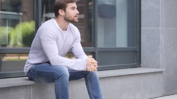 Vakava komea mies istuu toimiston ulkopuolella ja katselee ympärilleen
 - Materiaali, video