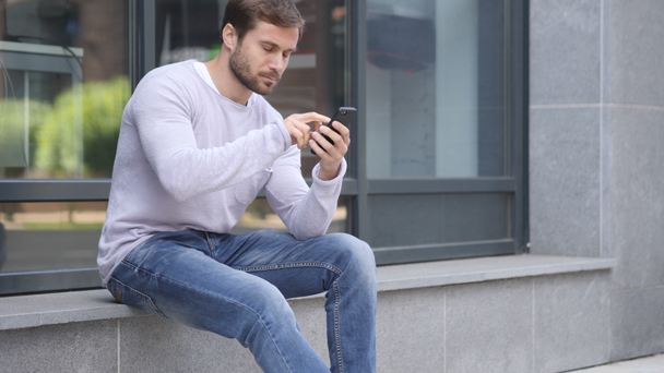 Szép ember használ Smartphone ül kívül Hivatal Online böngészés közben - Felvétel, videó