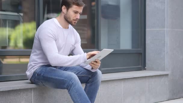 Hombre guapo usando tableta mientras está sentado fuera de la oficina, navegando en línea
 - Imágenes, Vídeo