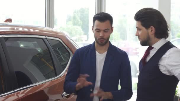 Two male friends discuaaing a new car at the dealership salon - Footage, Video