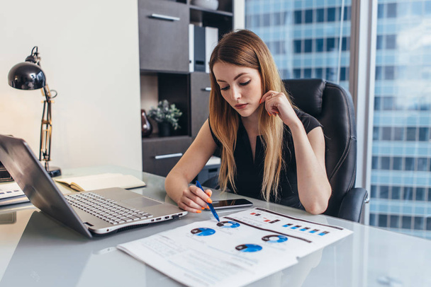 Mujer empresaria lee informe financiero analizando estadísticas apuntando a gráfico circular trabajando en su escritorio
 - Foto, imagen