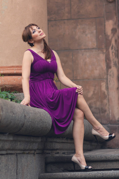 Eine bezaubernde Frau in lila Kleid sitzt auf den Stufen. Menschen - Foto, Bild