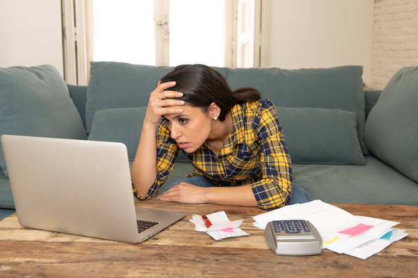 Young worried woman in stress banking and accounting debt bills, bank papers, expenses and payments with computer at home feeling desperate in a bad financial situation. - 写真・画像