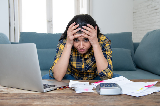 Young attractive woman worried at home banking and accounting home and credit card expenses with computer laptop doing paperwork in living cost stress and paying bills problem - Fotó, kép