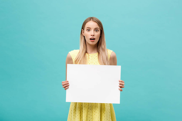 Portret van verbaasd jonge blonde vrouw leeg bord met kopie ruimte op blauwe studio achtergrond te houden. Weergegeven: geschokt verrassing gezicht. - Foto, afbeelding