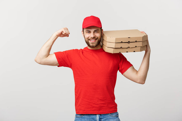 Concepto de entrega - Retrato de un hombre fuerte y guapo repartidor flexionando su músculo y sosteniendo paquetes de cajas de pizza. Aislado en Grey studio Background. Copiar espacio. - Foto, Imagen