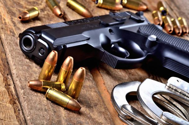 Pistolet 9mm, balles et menottes sur une vieille table en bois - vue sur le canon
 - Photo, image