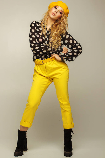 полный рост. красивая блондинка с профессиональным макияжем в желтых брюках и берете, позируя на сером фоне
 - Фото, изображение