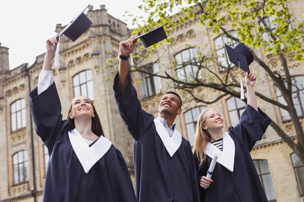Three happy students throwing their mortarboards in the air - Fotoğraf, Görsel