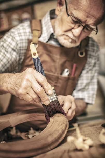elderly carpenter uses a brush on an unfinished chair - Fotó, kép